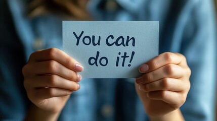 A person holding up an inspirational card with the words "You can do it!" written on it, representing determination and self-motivation in their daily life.