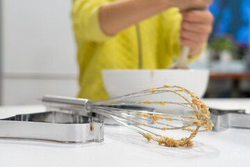 Whisks stained with dough seen from close up and an unrecognizable boy cooking in the background