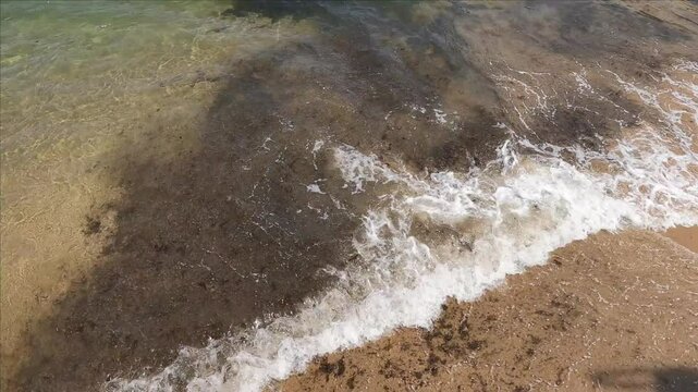 Confluencia de olas llegadas de distinto lado formando una V en la orilla del mar sobre playa de arena