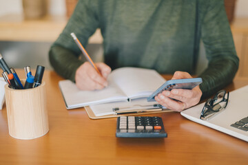 Office Worker Writing In Notebook While Using Smartphone And Calculator.