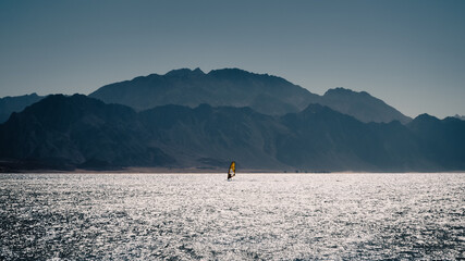 surfer rides in the Red Sea against the backdrop of the coast with high rocky mountains in Egypt...