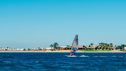 windsurfer rides in the sea on the background of the beach with palm trees and high rocky mountains in Egypt Dahab