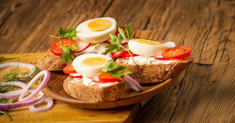 Sandwiches with tomatoes, onions and eggs lie on a wooden plate. Sandwiches on a wooden cutting board. Proper nutrition.