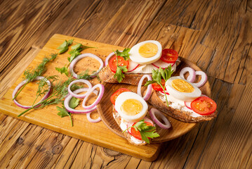 Sandwiches with tomatoes, onions and eggs lie on a wooden plate. Sandwiches on a wooden cutting board. Proper nutrition.