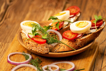 Sandwiches with tomatoes, onions and eggs lie on a wooden plate. Sandwiches on a wooden cutting board. Proper nutrition.