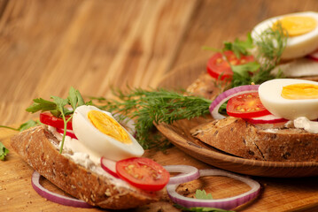 Sandwiches with tomatoes, onions and eggs lie on a wooden plate. Sandwiches on a wooden cutting board. Proper nutrition.