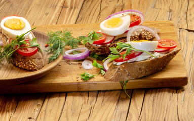 Sandwiches with tomatoes, onions and eggs lie on a wooden plate. Sandwiches on a wooden cutting board. Proper nutrition.