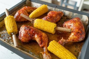 Oven baked chicken legs with corn on the cop fresh and homemade cooked on a baking tray. Ready to eat