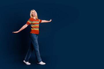 Photo of cheerful lovely senior woman wear striped stylish clothes walk empty space isolated on dark blue color background