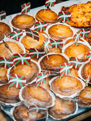 Display of freshly baked pastries, traditional from the Basque Country, each topped with small ikurriña flag, showcased in a bakery.