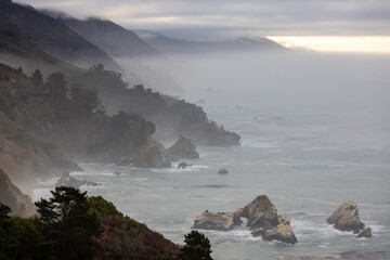 A breathtaking and serene view of the rugged, dramatic coastline of Big Sur, located in California, where mist softly envelops the lofty cliffs and gentle waves lap peacefully at the shore