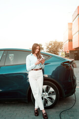 A young woman charges a car at a charging station near a supermarket. Charging an electric car....