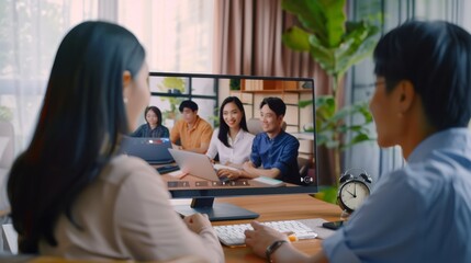 Colleagues engage in a video conference, discussing projects with teammates on a computer screen, fostering remote collaboration.