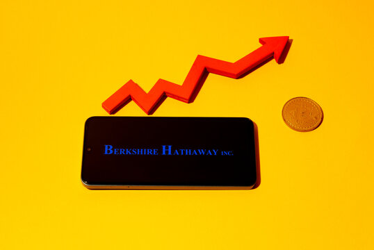 Kyoto city, Japan - august 22, 2024: Berkshire Hathaway logo on the smartphone screen and red chart arrow near bitcoin coin on yellow background.