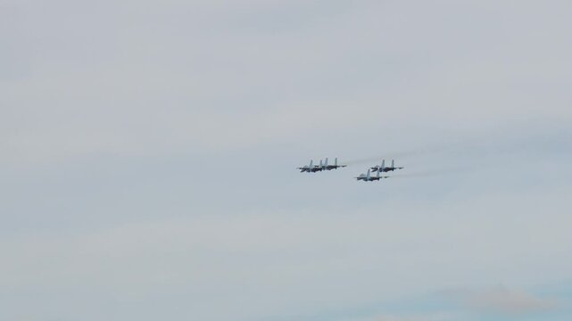 Four fighter jets flying in close formation, streaming across a vast, overcast sky. The aircraft maintain precise alignment, demonstrating aerial teamwork and precision