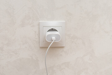 Charging cable in the outlet on white wall background