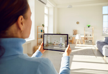 Back view of rental agent or female realtor taking photo on smart tablet device of stylish home...