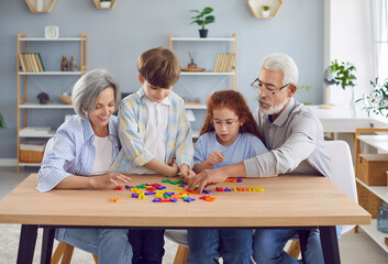Portrait of grandfather and grandmother teaching their grandchildren alphabet making words of...