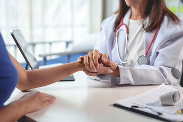 A female doctor holds a patient's hand to give encouragement in a consultation at a clinic or hospital. A doctor talks with a patient, gives hope. Mental health therapy for solace in treatment.