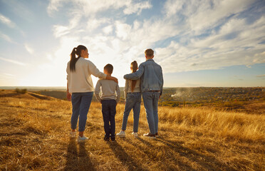 Back view of family of four hugging each other and looking into the distance enjoying sunset and...