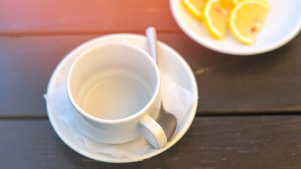 A white cup with a spoon on top of a napkin. A plate of lemons sits next to the cup