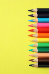 a group of multi-colored colorful large pencils on a yellow background