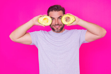 Funny Man hold half of fresh avocado isolated on pink background, studio portrait. The avocado. Healthy look. Portrait of handsome man hold avocado near his face.