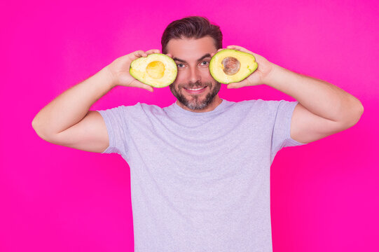 Funny Man hold half of fresh avocado isolated on pink background, studio portrait. The avocado. Healthy look. Portrait of handsome man hold avocado near his face.