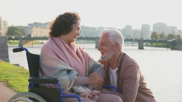 Senior woman in wheelchair walking with caregiver old man on road. Elderly family couple man supporting taking care of paralyzed woman in chair for people with disability outdoor. Rehabilitation