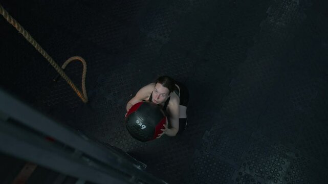 View from above of strong young woman doing wall ball squats during workout in fitness gym