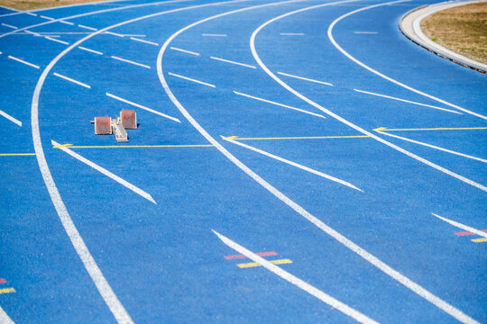 Vibrant blue running track with starting blocks, empty stadium, and textured background. Athletes prepare to race on a sunny day - Powered by Adobe