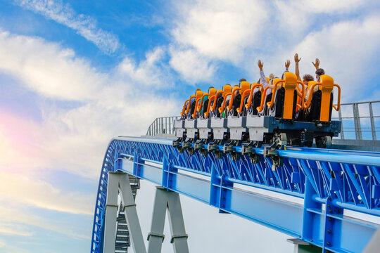 Roller coaster cart with people riding goes through the cart rises high into the air before descending sharply into steep dive against backdrop blue sky and clouds