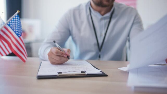 Close camera focus at Caucasian male sitting at desk and writing something on piece of paper. Filling in information. Checking voting blanks besides him. Confirming information. Poll worker.