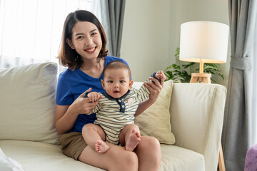 A woman is holding a baby on a couch. The baby is smiling and the woman is smiling back. Scene is happy and loving