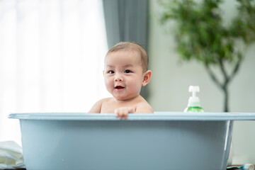 A baby is in a bathtub with a bottle of lotion next to it. The baby is smiling and looking at the camera