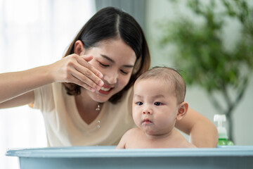 A woman is bathing a baby in a blue bathtub. The baby is smiling and the woman is smiling back. Concept of warmth and affection between the mother and child