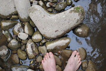 stones in river water and man's legs standing in point of view shot