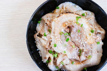 Donburi rice topped with chashu pork slices  in a black bowl.
