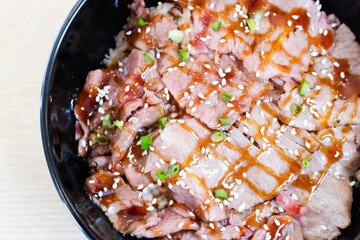 Donburi rice topped with smoked bacon slices in a black bowl.