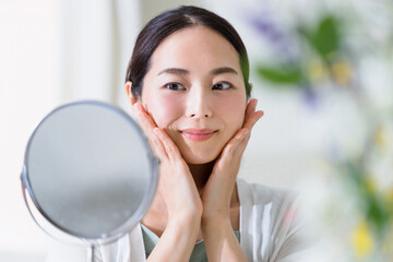 鏡を見てスキンケアをする女性（ビューティーイメージ）