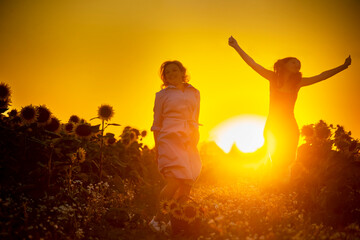 Fototapeta premium A mother and daughter on a dirt road in a field of sunflowers at sunset are having fun and holding hands.