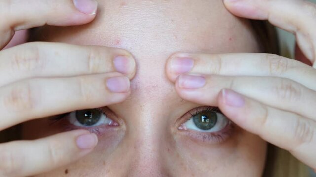 Close up of a young caucasian woman frowning touching the forehead showing wrinkles on her face on a grey background. The inter-brow wrinkle on the forehead. Skin care. Beauty concept