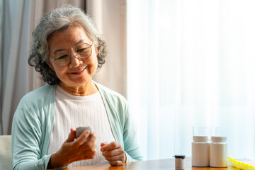 Asian senior mature woman patient with diabetes using medical device glucometer checking glucose in blood by herself in bedroom at home. Elderly people self-care and daily health check concept.