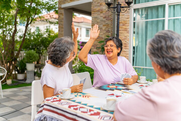 Obraz premium Group of Happy Asian senior mature women relax and enjoy indoor lifestyle meeting party together at home. Elderly retired woman friends having fun playing card together at home garden in summer day.