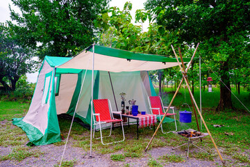 Camping tents at night, vintage cabin tents,  Antique lanterns, retro chairs, and outdoor coffee-making facilities on wooden tables in a forest