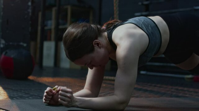 Young sportswoman standing in plank, leaning on her elbows and taking starting position, then lying on mat and relaxing during gym workout