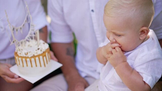 Unrecognized parents hold a cake in front of their baby. Mother shows a cake to her child. Family celebrating first kid's birthday. Close up.
