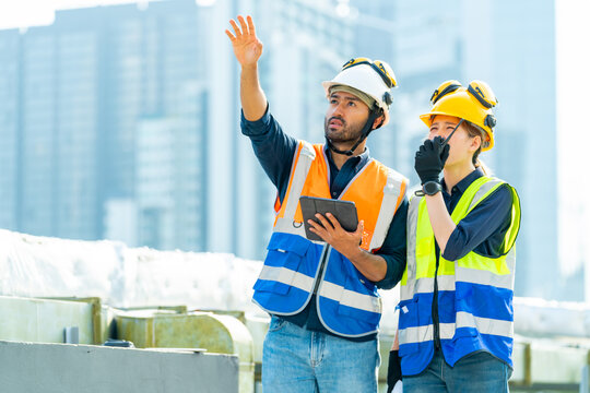 Asian man and woman teamwork engineer working on digital tablet and speaking on two way radios at construction site building rooftop. Architecture inspector inspect building exterior structure system.