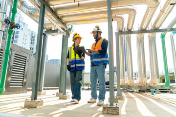 Professional Asian man and woman teamwork engineer in safety uniform working at outdoor construction site rooftop. Industrial technician worker maintenance checking building exterior plumbing systems.