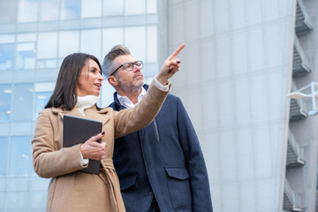 Confident business duo discussing strategy outside office building in city, using tablet for...